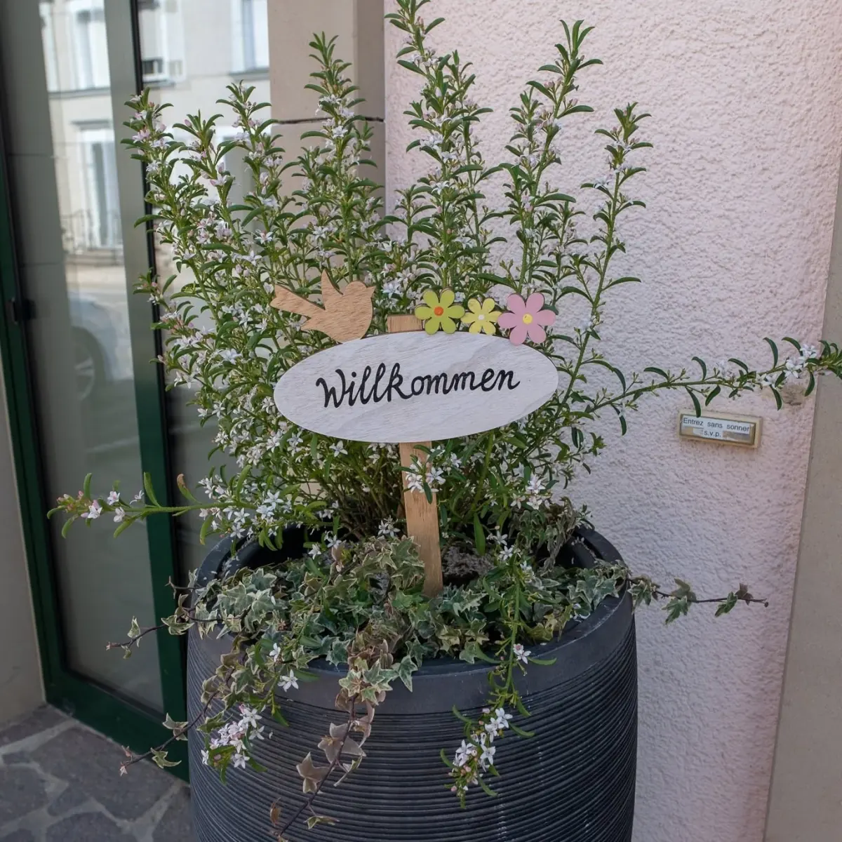 Blumentopf am Eingang mit einem Holzschild „Willkommen“