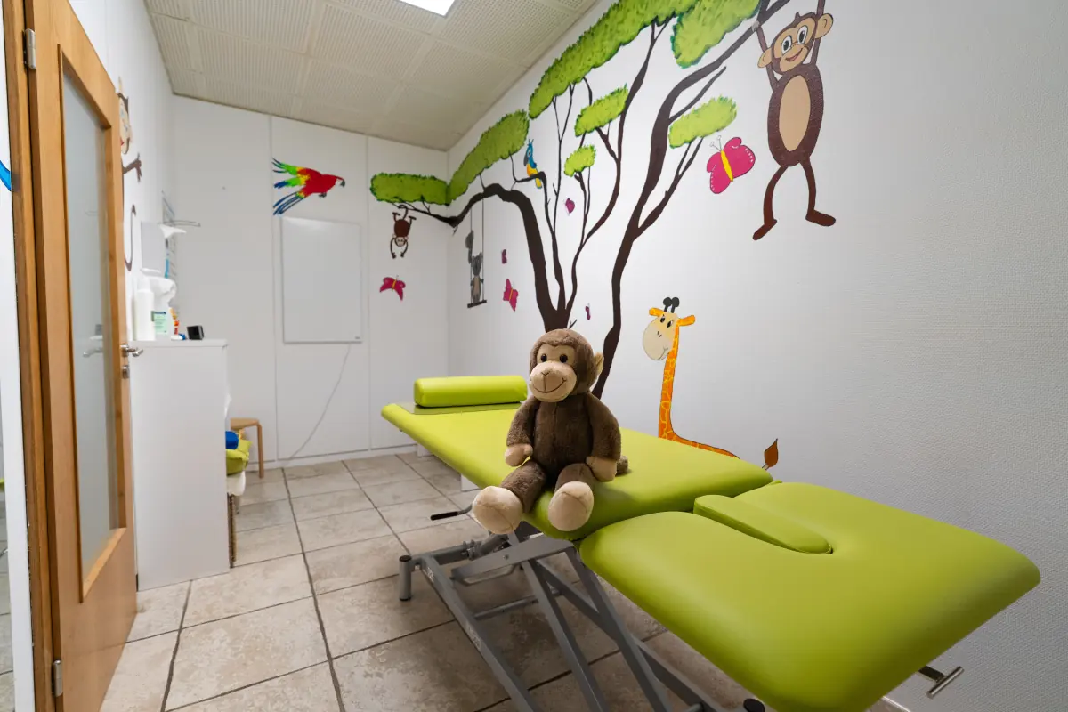 Ein Plüschaffe sitzt auf der grünen Liege im Kinderraum